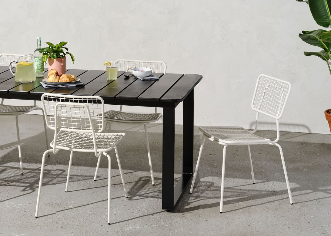Grey outdoor setting featuring a black slat top table surrounded by white metal chairs